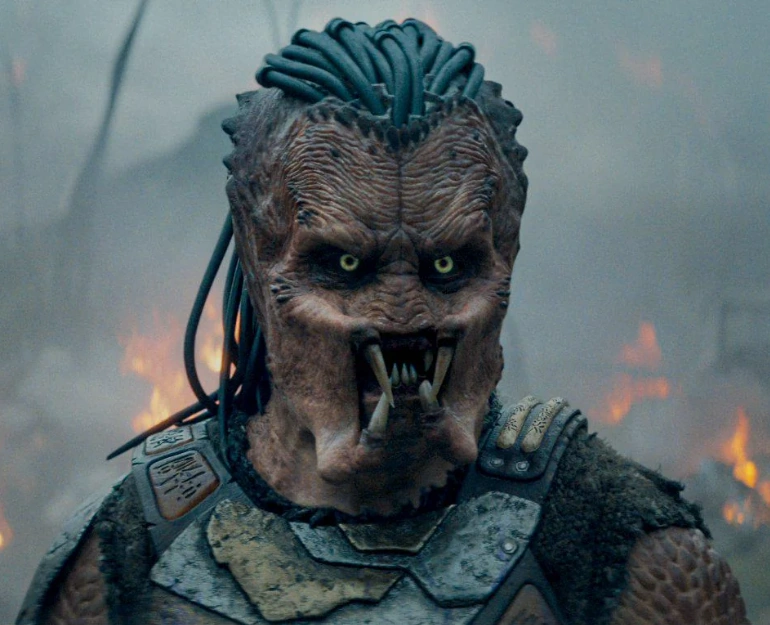 Dek the young Predator warrior from Predator: Badlands (2025) standing in alien wasteland battle scene.